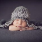 צילומי ניו בורן לתינוק בן שבוע עם רקע אפור וכובע אפור תואם