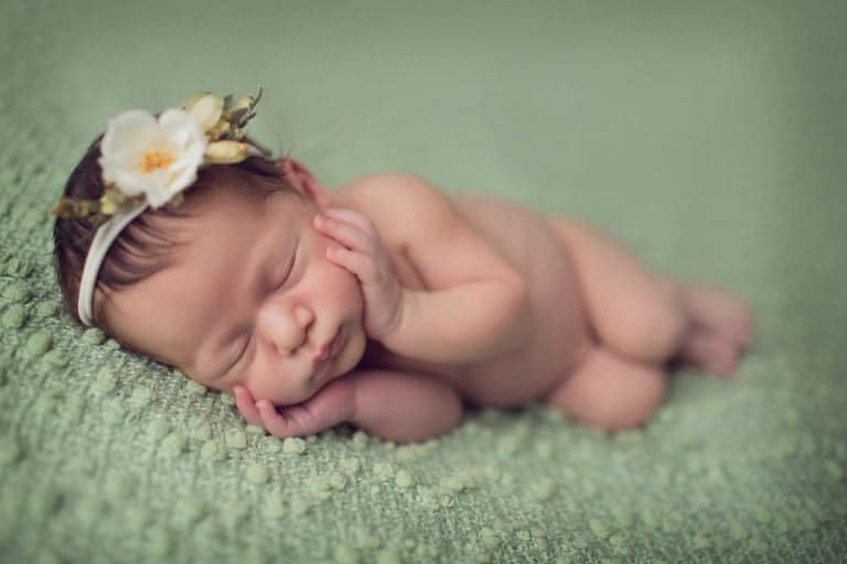 צילומי ניובורן לתינוקת על רקע שמיכה ירוקה עם סרט ראש לבן