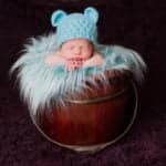 צילום ניובורן לתינוק בן שבוע שמונח בסלסלת עץ עם פרווה רכה וכובע דובון תכלת