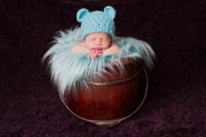 צילום ניובורן לתינוק בן שבוע שמונח בסלסלת עץ עם פרווה רכה וכובע דובון תכלת