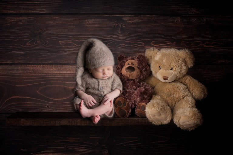 צילום ניובורן של תינוק בתלבושת דובון יושב על מדף עם דובונים