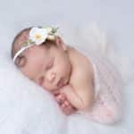 תמונה של תינוקת ישנה בנעימים בעיטוף לבן וסרט ראש לבן