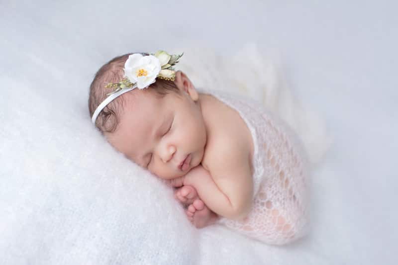 תמונה של תינוקת ישנה בנעימים בעיטוף לבן וסרט ראש לבן