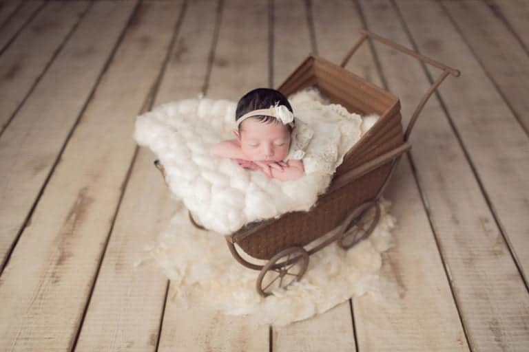 תינוקת בת חמישה ימים ישנה בעגלת וינטג׳ עם שמיכה לבנה בזמן צילומי ניובורן בסטודיו יעל אלעד