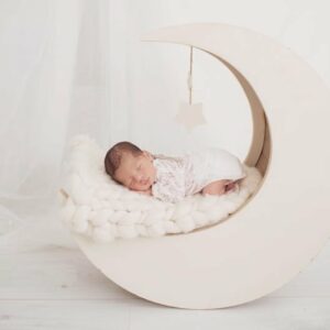 צילומי ניובורן לתינוקת שרק נולדה עם בגד לבן ישנה על הירח