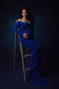 צילום הריון לסיון שלובשת שמלה בכחול רויאל ויושבת על סולם