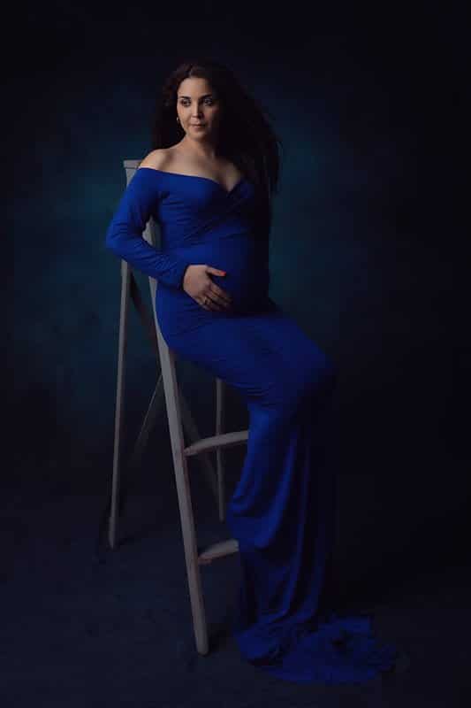 צילום הריון לסיון שלובשת שמלה בכחול רויאל ויושבת על סולם